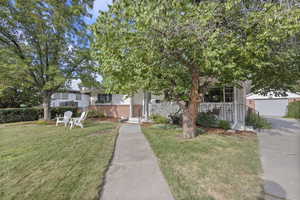 View of property hidden behind natural elements featuring a front yard and brick siding