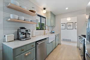 Kitchen featuring green cabinets, decorative backsplash, light wood-type flooring, appliances with stainless steel finishes, and open shelves