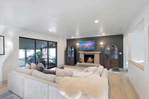 Living area featuring light wood-style floors, recessed lighting, and a warm lit fireplace
