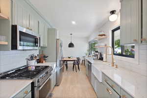 Kitchen featuring backsplash, stainless steel appliances, light wood-style floors, hanging light fixtures, and recessed lighting