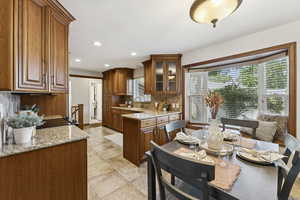 Kitchen with recessed lighting, decorative backsplash, brown cabinetry, and light stone counters