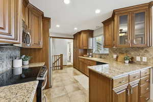 Kitchen featuring decorative backsplash, appliances with stainless steel finishes, brown cabinetry, light stone counters, and recessed lighting