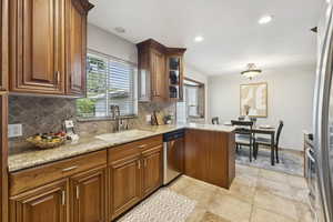 Kitchen featuring backsplash, light stone countertops, recessed lighting, stainless steel appliances, and a peninsula