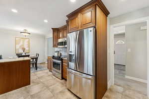 Kitchen with stainless steel appliances, recessed lighting, brown cabinetry, backsplash, and light tile patterned floors