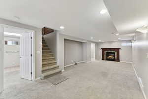Below grade area with carpet floors, a glass covered fireplace, stairs, healthy amount of natural light, and recessed lighting