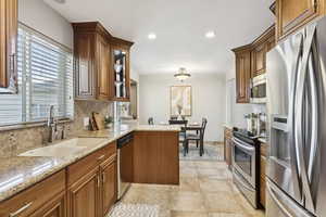 Kitchen with stainless steel appliances, backsplash, brown cabinets, light stone countertops, and recessed lighting