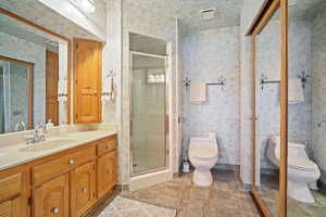 Bathroom featuring vanity, a stall shower, and wallpapered walls.