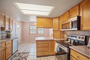 Kitchen with tasteful backsplash, stainless steel appliances, light tile patterned floors, and a peninsula