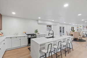 Kitchen with stainless steel gas range, a breakfast bar, light wood-type flooring, recessed lighting, and an island with sink