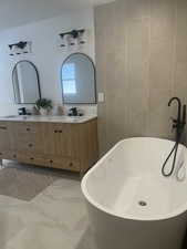 Bathroom featuring marble look tiles, double vanity, tile walls, and a freestanding bath