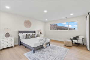 Bedroom with a barn door, recessed lighting, and light wood-style flooring