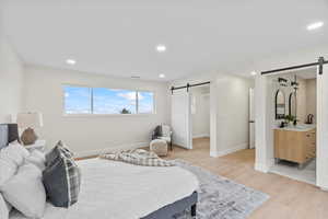 Bedroom featuring a barn door, light wood-style floors, recessed lighting, a walk in closet, and ensuite bathroom