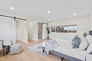Bedroom with a barn door, recessed lighting, wood finished floors, and connected bathroom