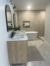 Full bath with double vanity, a soaking tub, and marble look tiles