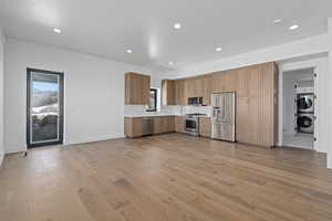 Kitchen with estacked washer and dryer, stainless steel appliances, light wood-style flooring, backsplash, and light countertops