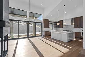 Kitchen featuring high vaulted ceiling, light countertops, open shelves, a chandelier, and wall chimney range hood