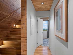 Hall featuring light wood-style flooring, a sauna, wood ceiling, stairway, and wooden walls
