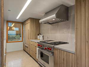 Kitchen with designer stove, wall chimney range hood, light countertops, light tile patterned floors, and tasteful backsplash