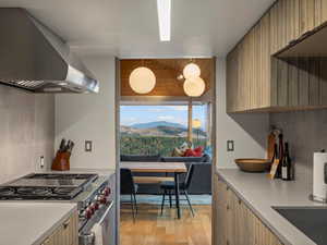 Kitchen with range hood, stainless steel range with gas cooktop, light wood finished floors, light countertops, and a mountain view