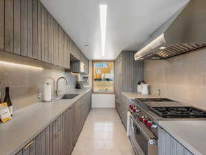 Kitchen featuring range hood, double oven range, backsplash, light countertops, and light tile patterned flooring
