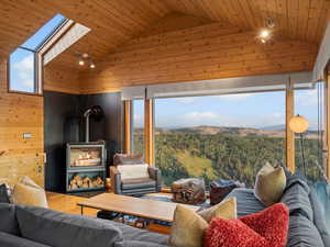 Living area with wooden walls, a wood stove, a forest view, wood ceiling, and high vaulted ceiling