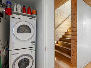 Laundry room featuring stacked washer / dryer, light wood-type flooring, electric panel, and wood walls