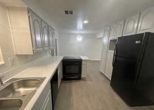 Kitchen with black appliances, light wood-type flooring, a peninsula, light countertops, and recessed lighting