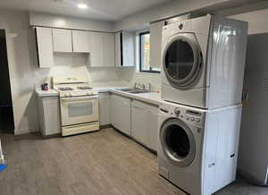Kitchen featuring white gas range, stacked washer / drying machine, light wood finished floors, light countertops, and white cabinetry