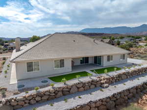 Rear view of property featuring a patio area, stucco siding, terraced rear with stone retaining walls and step down ladders, and a chimney to the wood-burning fireplace in the family room.  Concrete sidewalks surround the home.