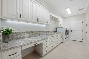 Main Laundry room with granite countertops, soft-close cabinetry, cabinet space, and ornamental molding with built-in ironing board and entrance to garage.