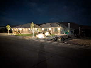 Ranch-style house with concrete driveway, a chimney, an attached 5+ car garage with two 18 ft doors, and stone siding plus exterior night lighting
