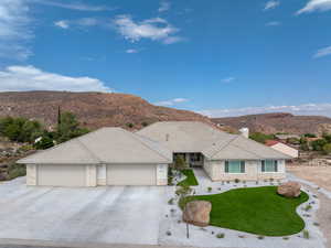 Ranch-style house featuring stone siding, a mountain view, an attached5+ car garage, concrete driveway, Low E WIndows, artificial turf & floral bushes.