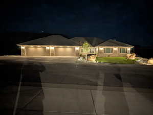 Ranch-style house with stone siding, a 5+ car garage with two 18' doors, driveway, and a tiled roof plus exterior night lighting