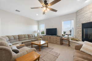 Main Family room with light colored carpet, healthy amount of natural light, a floor to ceiling stone fireplace, recessed lighting, ceiling fan and built in cabinet.