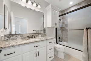 Full bath with vanity and shower / bath combination with sliding glass shower doors, granite countertops and soft-close cabinetry and tile flooring.