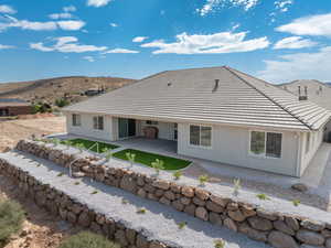 Rear view of house with a covered patio, step down terraced low-water landscaping and stucco siding with stone retaining walls and step down ladders.  Concrete sidewalks surround the home.
