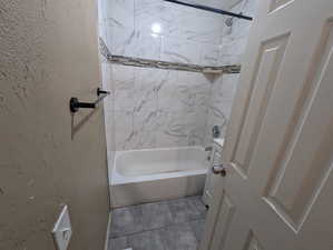 Full bathroom with a textured wall and washtub / shower combination