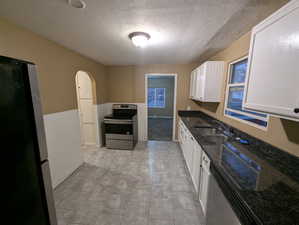 Kitchen with appliances with stainless steel finishes, a textured ceiling, arched walkways, dark stone countertops, and white cabinets