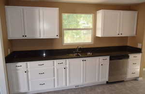 Kitchen with stainless steel dishwasher, white cabinets, light tile patterned floors, and dark stone counters