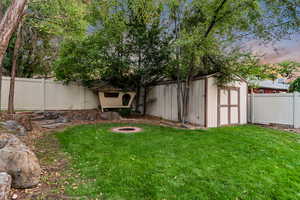 Yard at dusk featuring a fenced backyard, a storage shed, and an outdoor fire pit