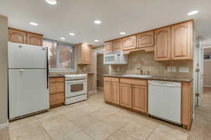 Kitchen with white appliances, recessed lighting, tasteful backsplash, light tile patterned floors, and light brown cabinetry