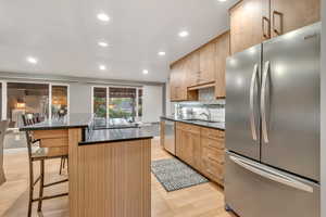 Kitchen with appliances with stainless steel finishes, recessed lighting, tasteful backsplash, a breakfast bar, and a kitchen island