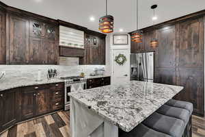 Kitchen featuring stainless steel appliances, decorative backsplash, a kitchen breakfast bar, light stone countertops, and recessed lighting