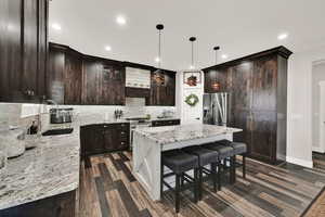 Kitchen with tasteful backsplash, appliances with stainless steel finishes, dark brown cabinets, light stone counters, and a kitchen island