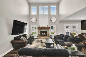 Living room featuring wood finished floors, a stone fireplace, and a towering ceiling