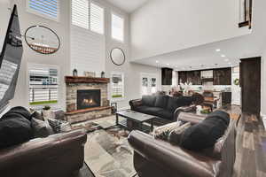 Living area with wood finished floors, healthy amount of natural light, a high ceiling, a stone fireplace, and recessed lighting