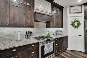 Kitchen featuring stainless steel appliances, light stone countertops, decorative backsplash, and dark brown cabinetry