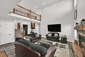 Living room featuring a towering ceiling, a stone fireplace, recessed lighting, dark wood-style floors, and stairway