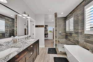 Bathroom with a stall shower, a freestanding bath, double vanity, wood finished floors, and recessed lighting