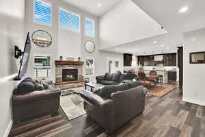 Living area featuring recessed lighting, dark wood finished floors, plenty of natural light, a stone fireplace, and a high ceiling